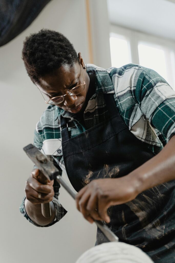 African-American sculptor in glasses focused on chiseling a sculpture indoors.